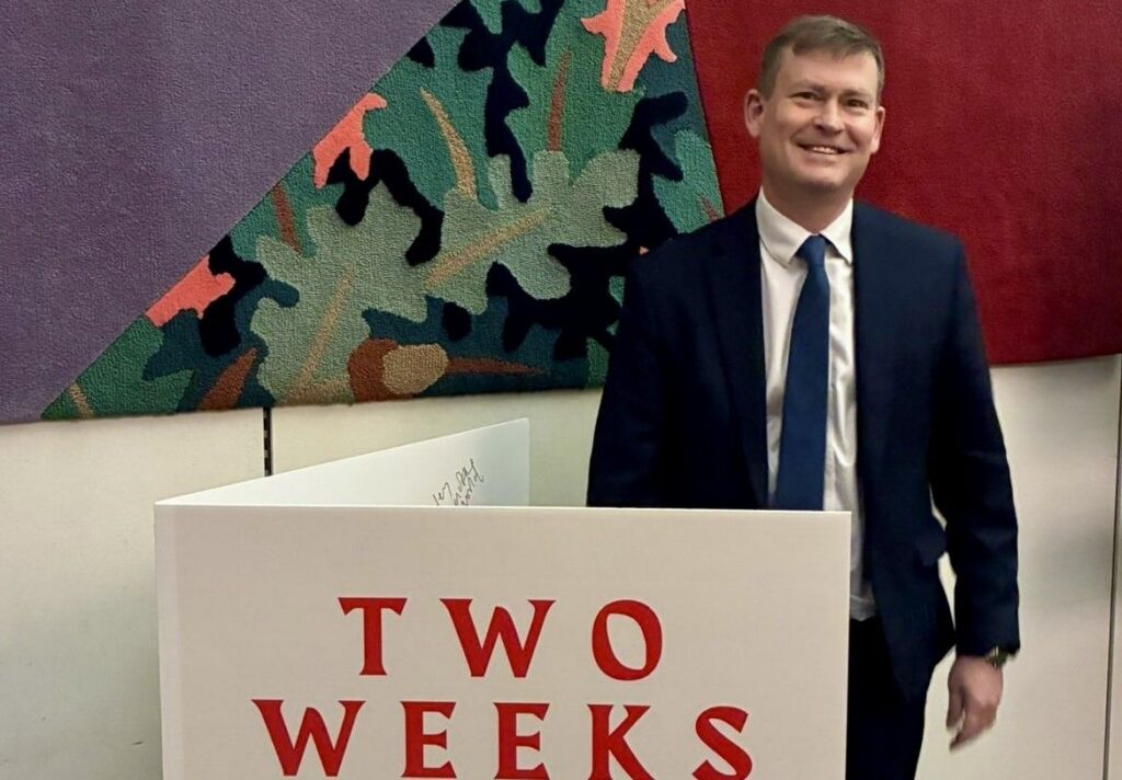 Justin Madders MP pictured at a Dad Shift event standing behind a mock-up 'congratulations' card highlighting the message that two weeks' leave isn't enough for new dads and non-birthing partners.